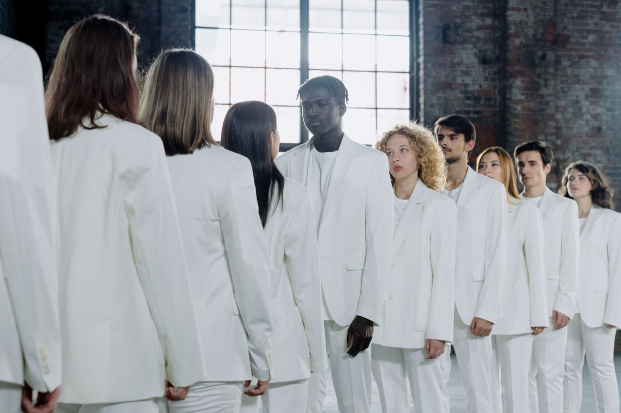 Multicultural group of individuals in white suits standing in a lined arrangement inside an industrial space.